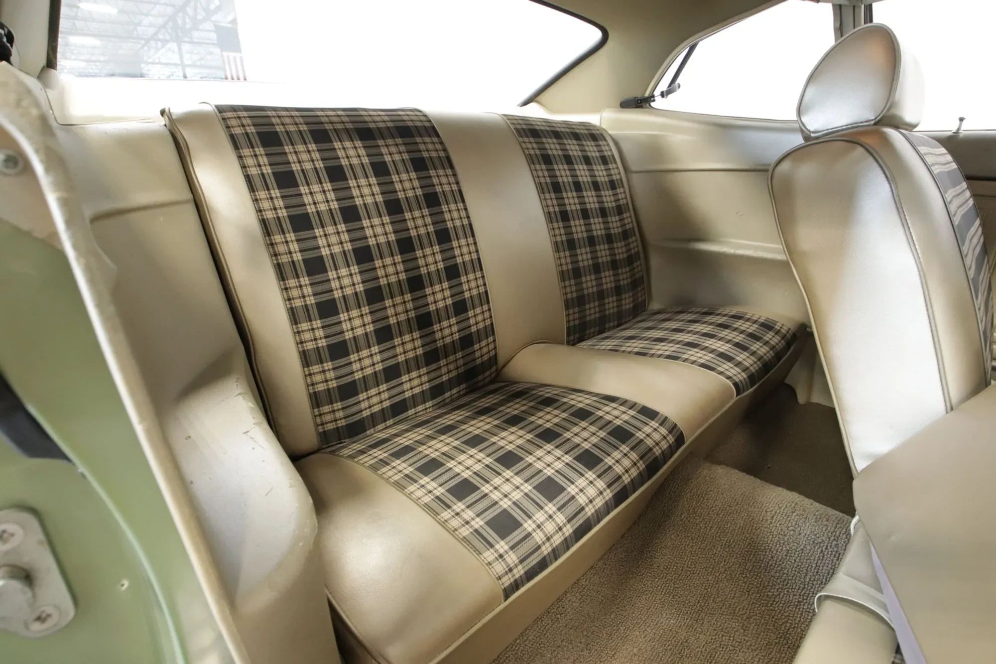 Back seat of a light green 1970 Ford Maverick with beige vinyl upholstery with black Tartan cloth inserts