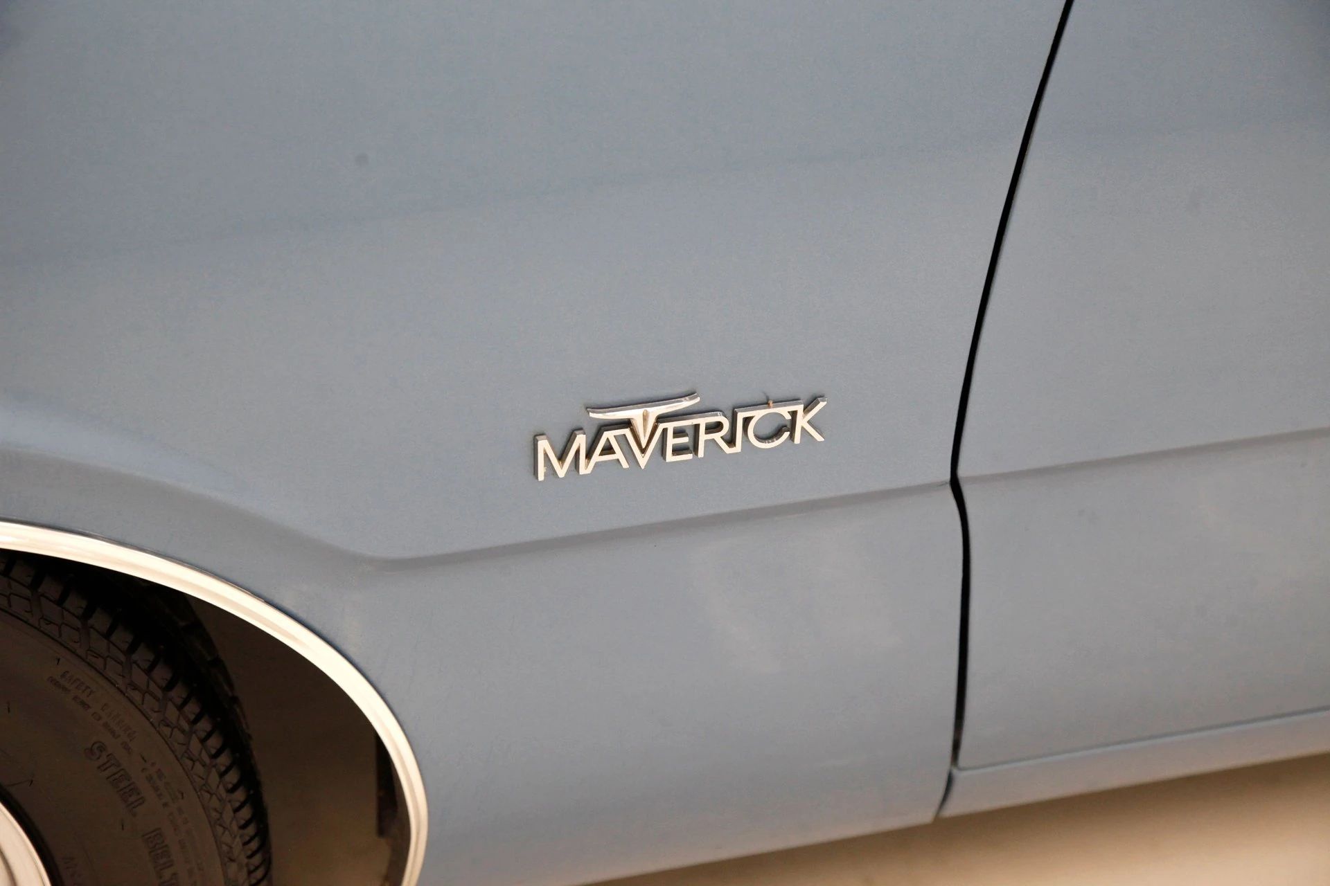 Maverick badge on the left from fender of a light blue metallic 1970 ford Maverick