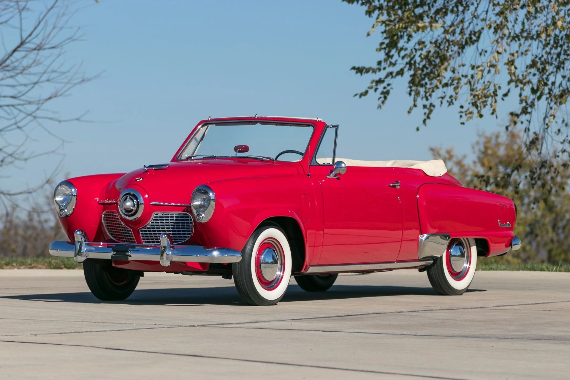 Left front 3q view of a red 1951 Studebaker Champion convertible with its top down, parked outside in the sun