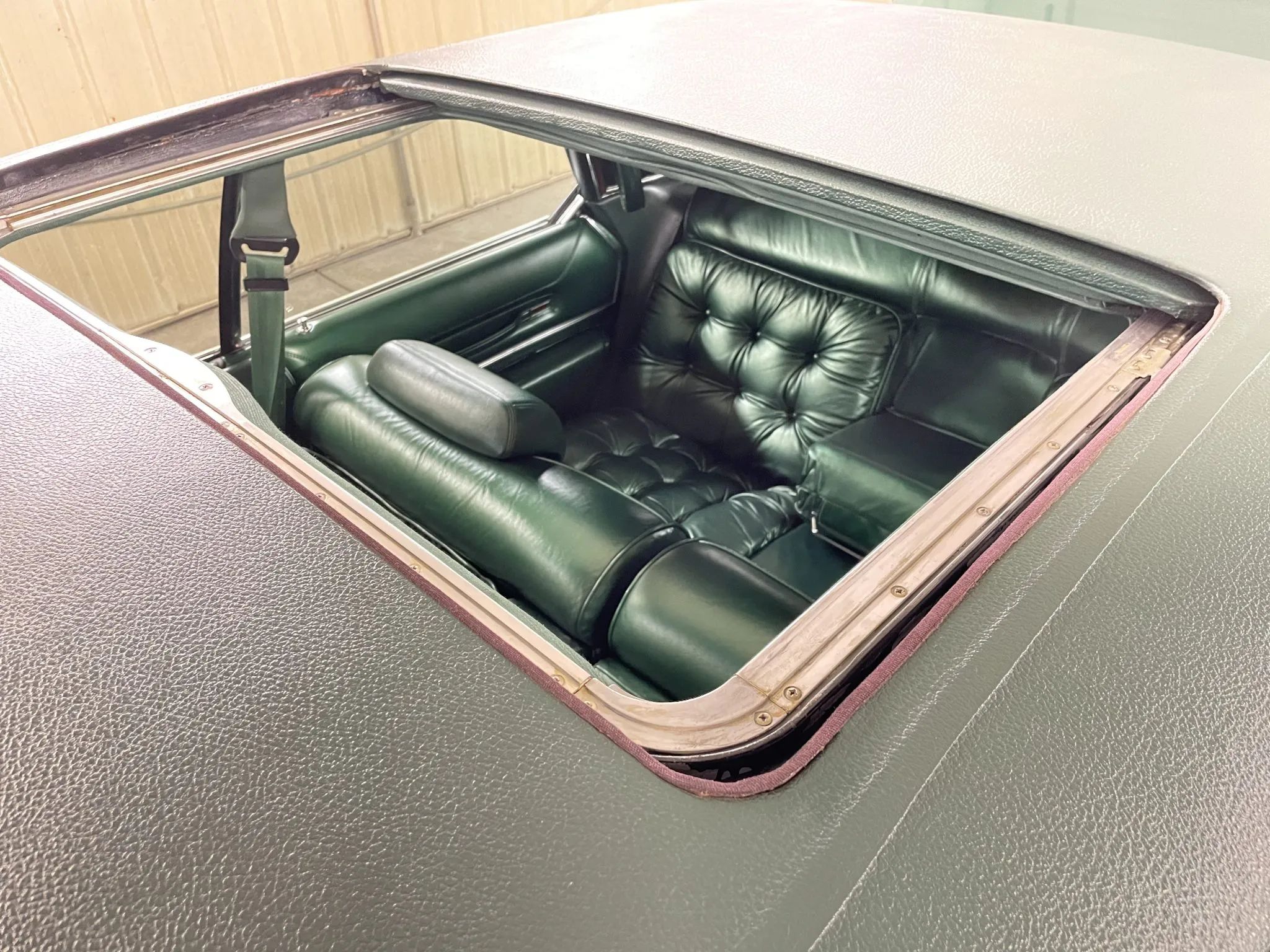 Back seat of a 1975 Imperial LeBaron four-door hardtop with dark green leather upholstery, seen through the open sunroof