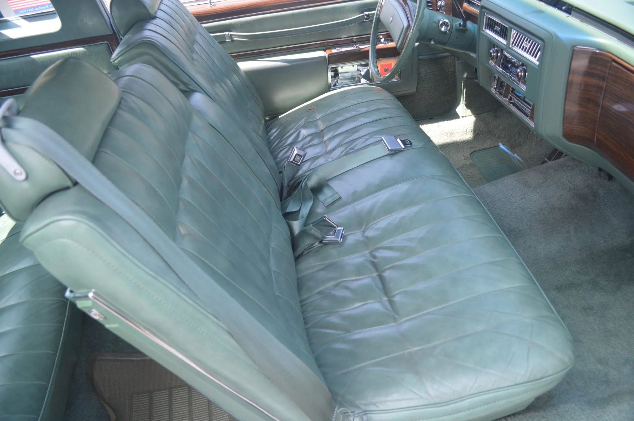 Front seat of a 1977 Cadillac Coupe de Ville with light green leather, viewed through the passenger door
