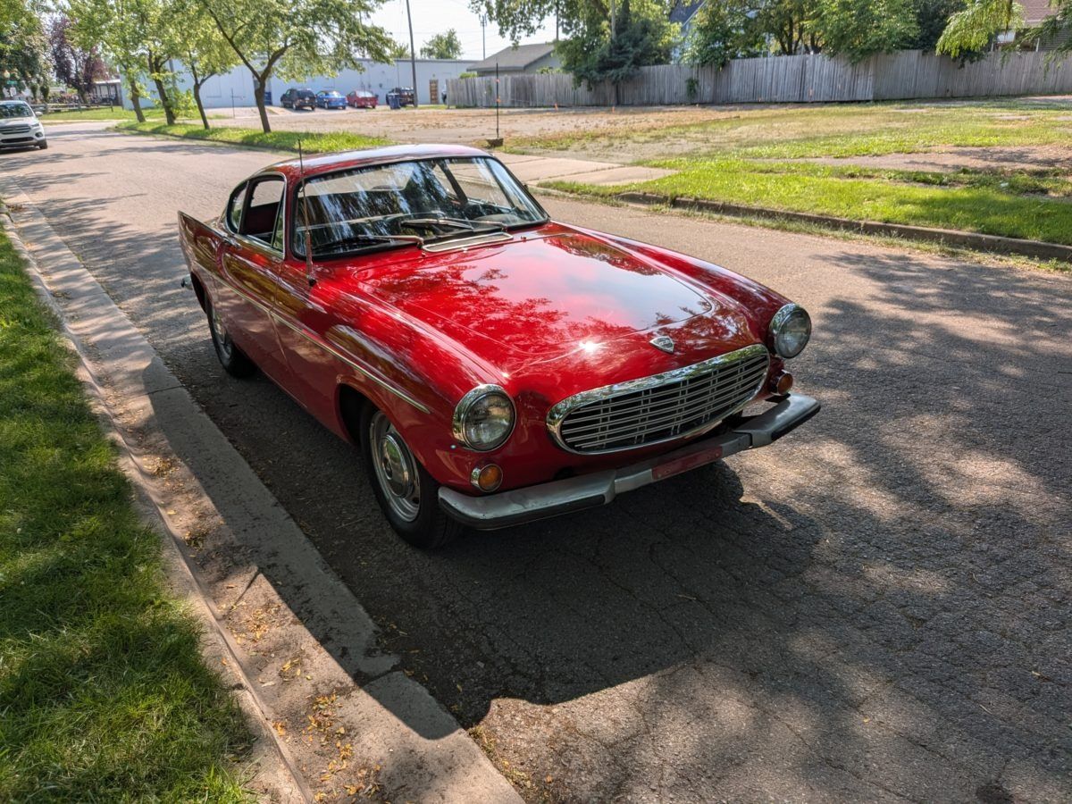 Another photo of the red Volvo 1800S on a tree-lined street