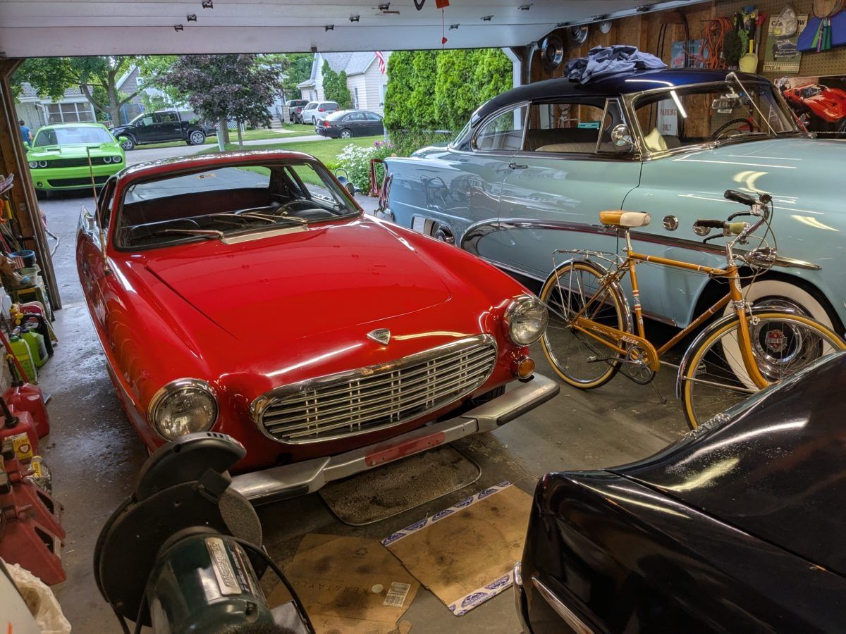 The 1967 Volvo 1800S in the garage next to a bicycle and a blue 1950s Buick