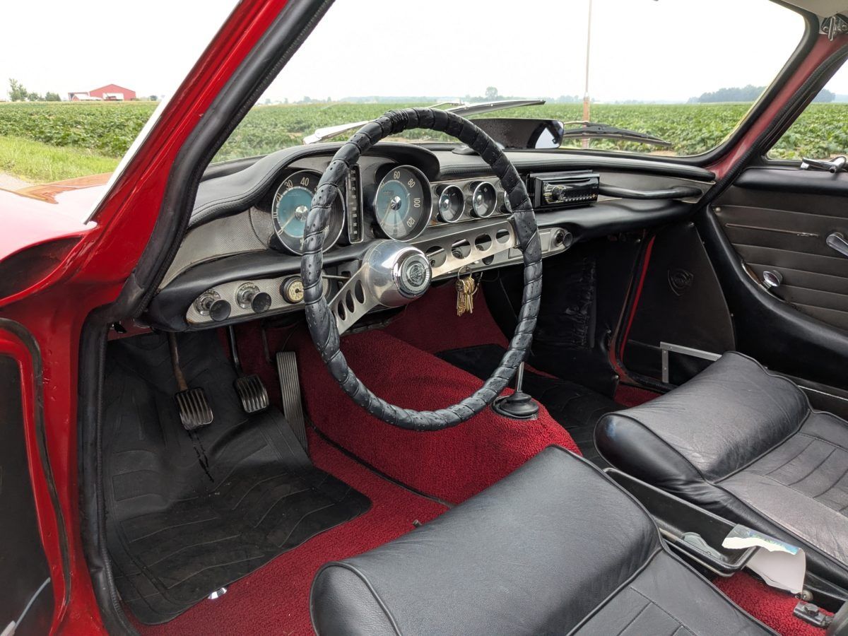 Interior of the 1967 Volvo 1800S coupe, with black seats and red carpeting plus a leather-wrapped steering wheel