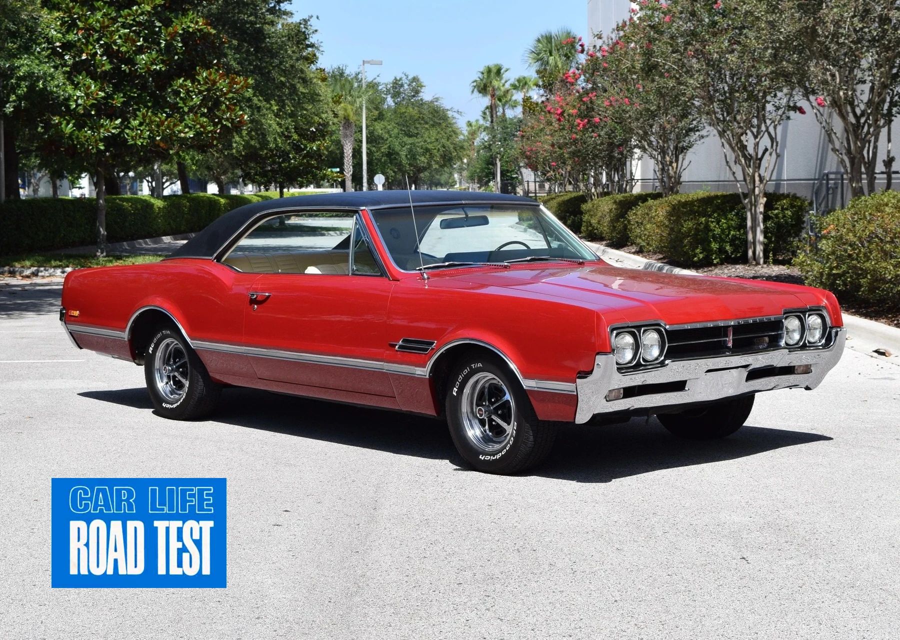 Photo of a red 1966 Oldsmobile Cutlass 4-4-2 hardtop with a black vinyl roof and Super Stock wheels, with a blue banner in the lower left corner reading "CAR LIFE ROAD TEST"