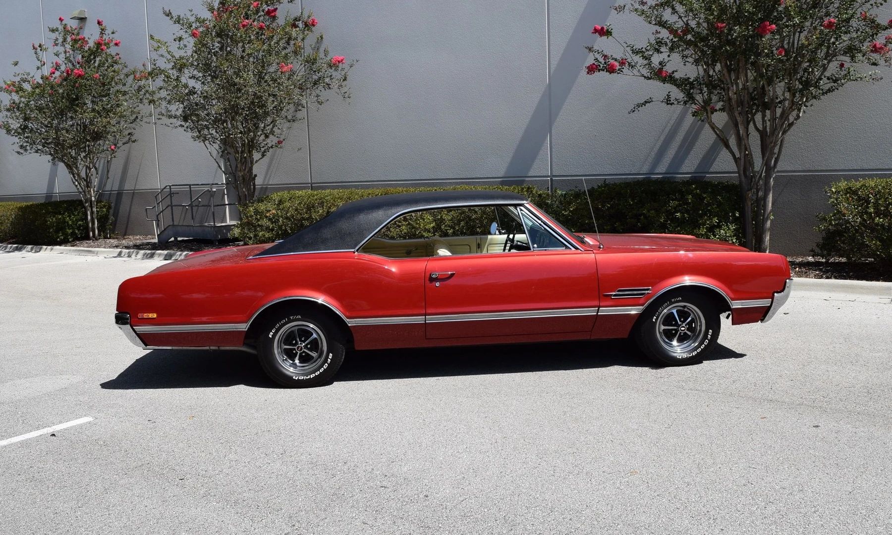 Right side view of a red 1966 Oldsmobile 4-4-2 hardtop with a black vinyl roof