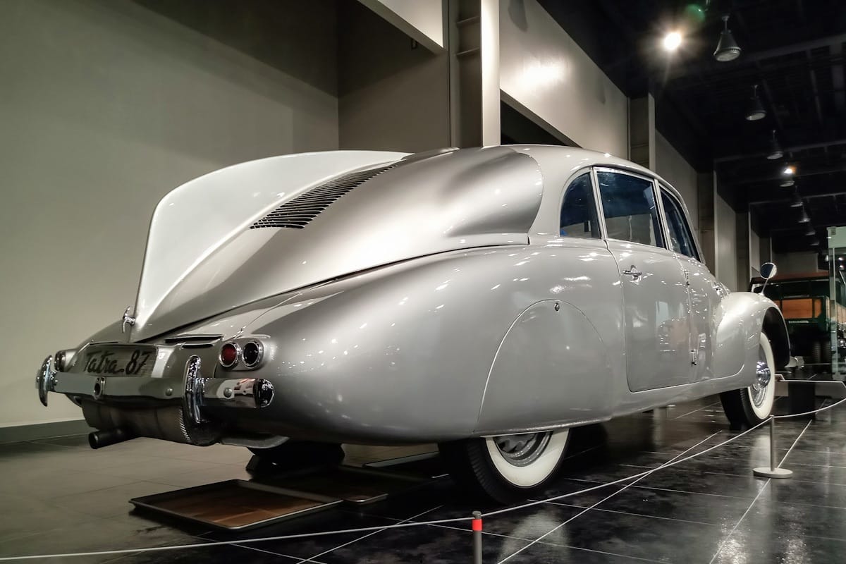 Photo of a silver 1946 Tatra 87, with a big dorsal fin, in an indoor museum space