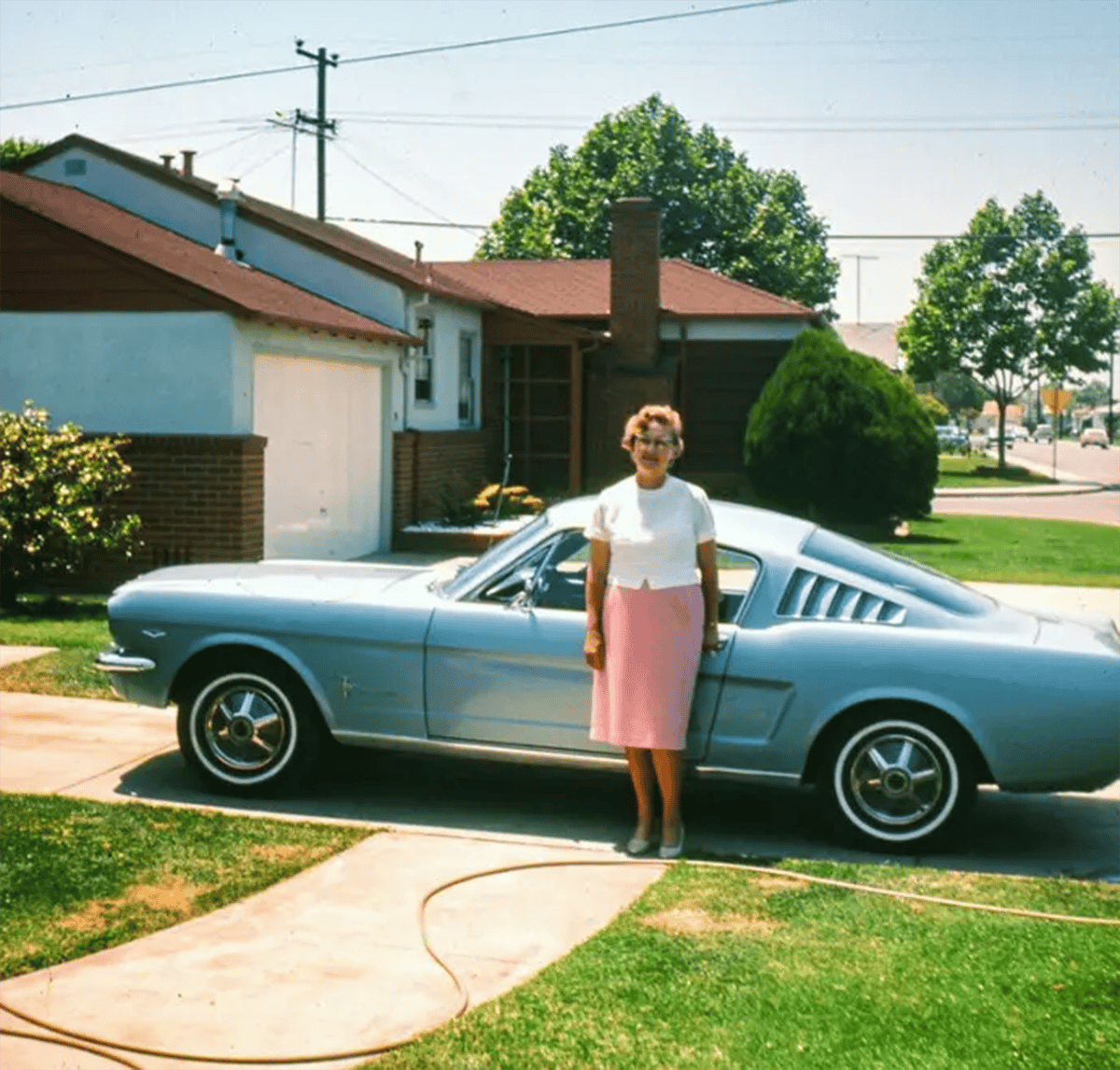 Classic American Fastbacks Of The 1960s & 1970s In Vintage Photos 1 Vintage photo of a woman in a white top and a pink skirt leaning on a light blue Ford Mustang fastback