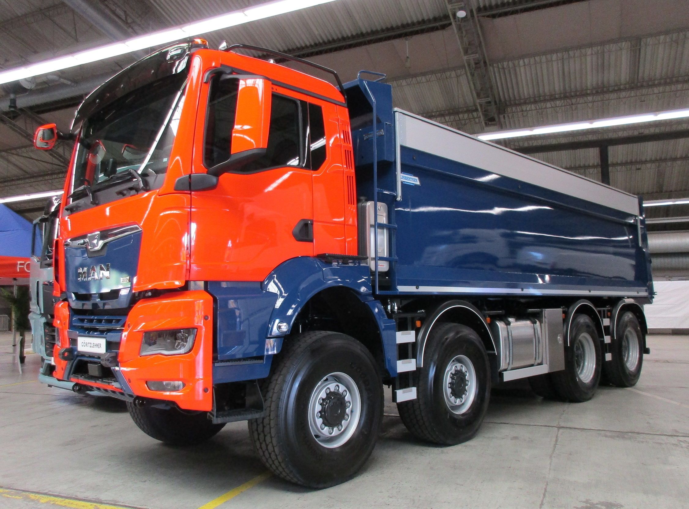 CC Global: 2025 MAN TGS 46.520 8x8 Wide Spread – The Traton Group's King Off The Road 1 Harry Remmink photo of an orange and blue 2025 MAN TGS 46.520 8x8 Wide Spread truck in a warehouse