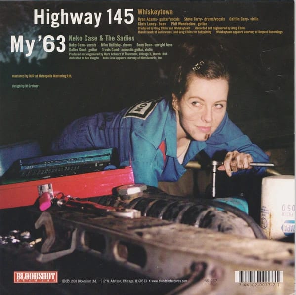 Back sleeve art of Highway 145/My '63 single, showing Neko Case in a blue mechanic's jumpsuit leaning over the hood of a 1963 Rambler. She has a wrench in her hand and grease on her hands and face