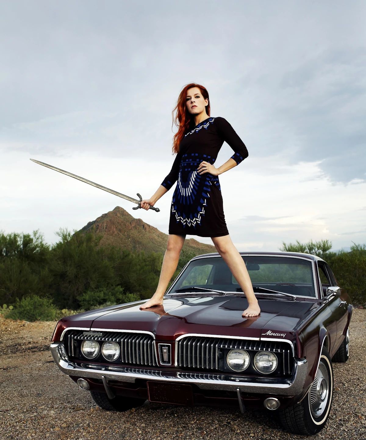 Photo of singer Neko Case standing on the hood of a 1967 Mercury Cougar, holding a sword