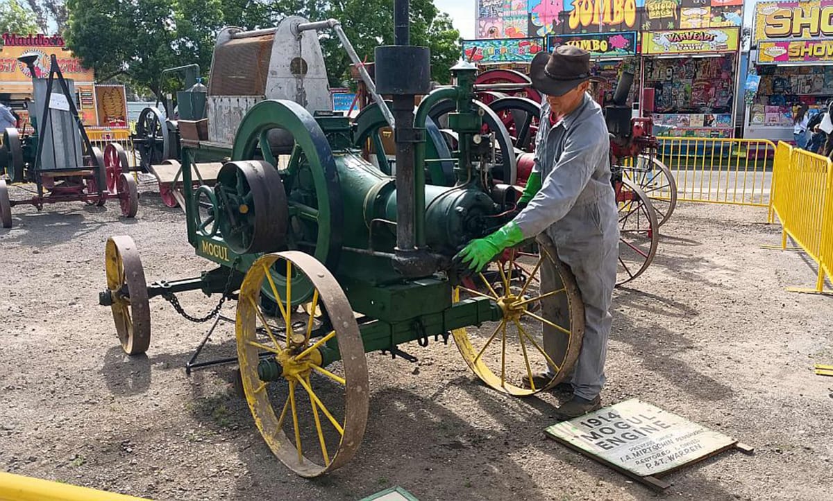 A man in blue overalls standing by 1914 Mogul engine display at the Geelong show in Victoria. 