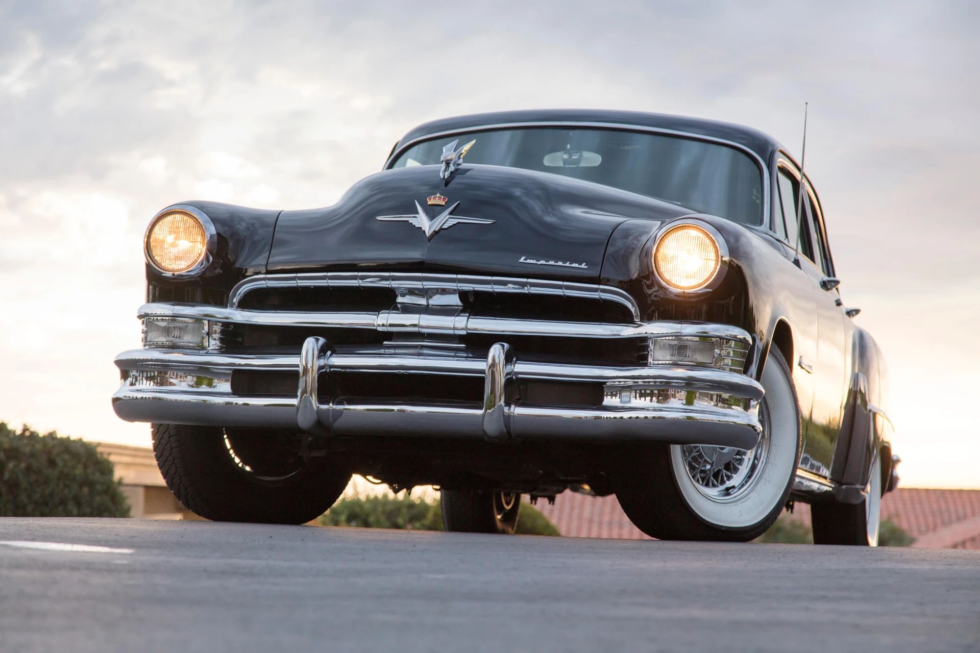 Low-angle front view of a black 1953 Chrysler C-58 Custom Imperial sedan with its headlights on, photographed at sunset