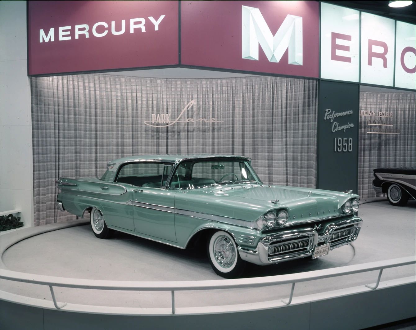 Vintage press photo of a green 1958 Mercury Park Lane four-door hardtop at a car show booth
