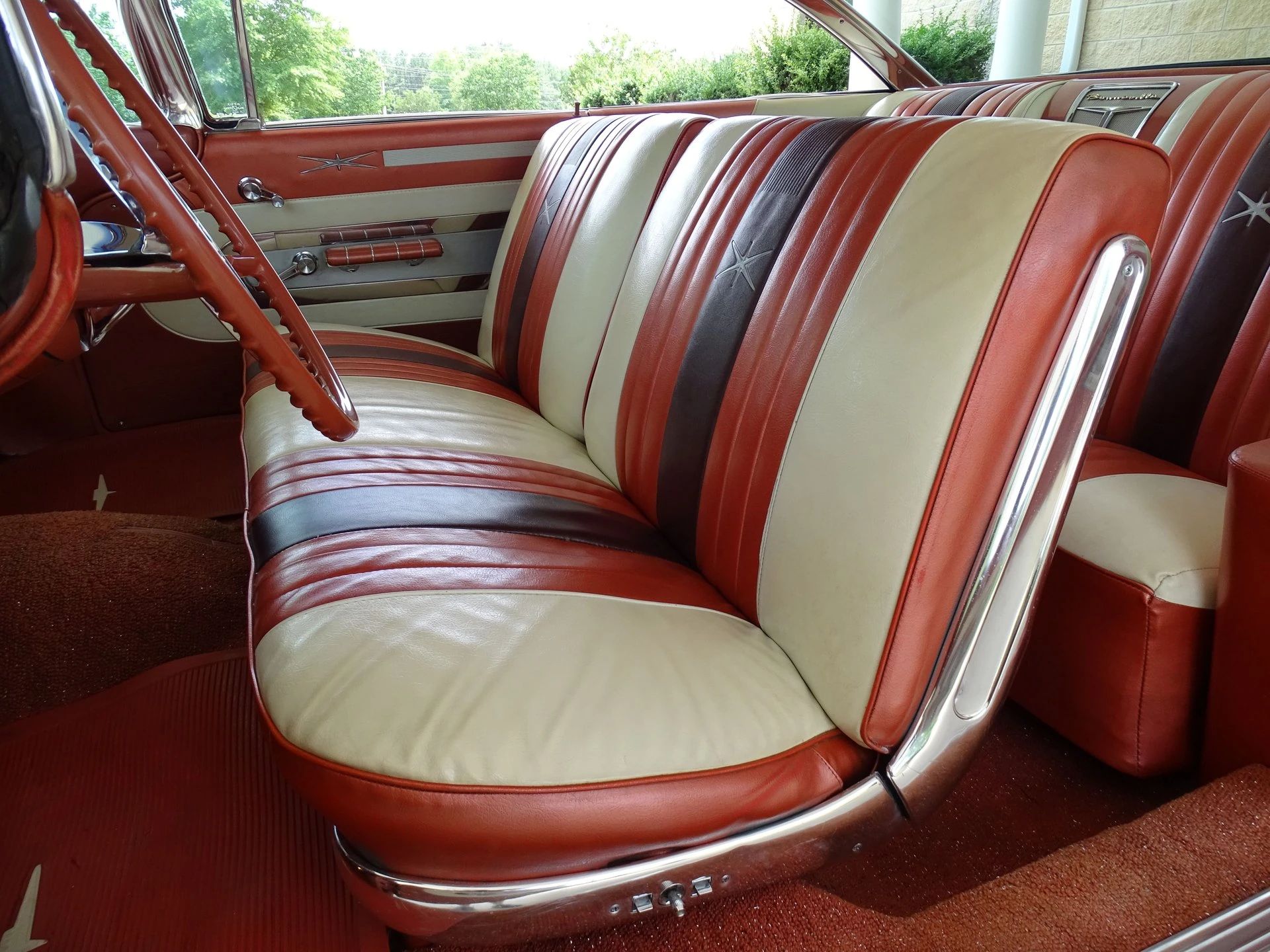 Front seat of a 1959 Pontiac Bonneville two-door hardtop with tri-tone white, red, and brown upholstery, seen through the driver's door