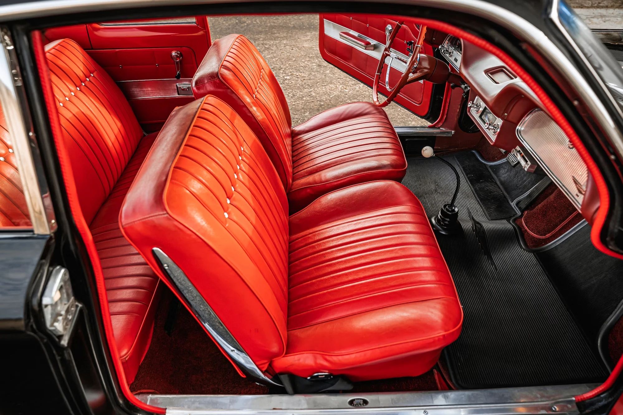Red vinyl front bucket seats in a 1962 Chevrolet Corvair, seen through the open passenger door