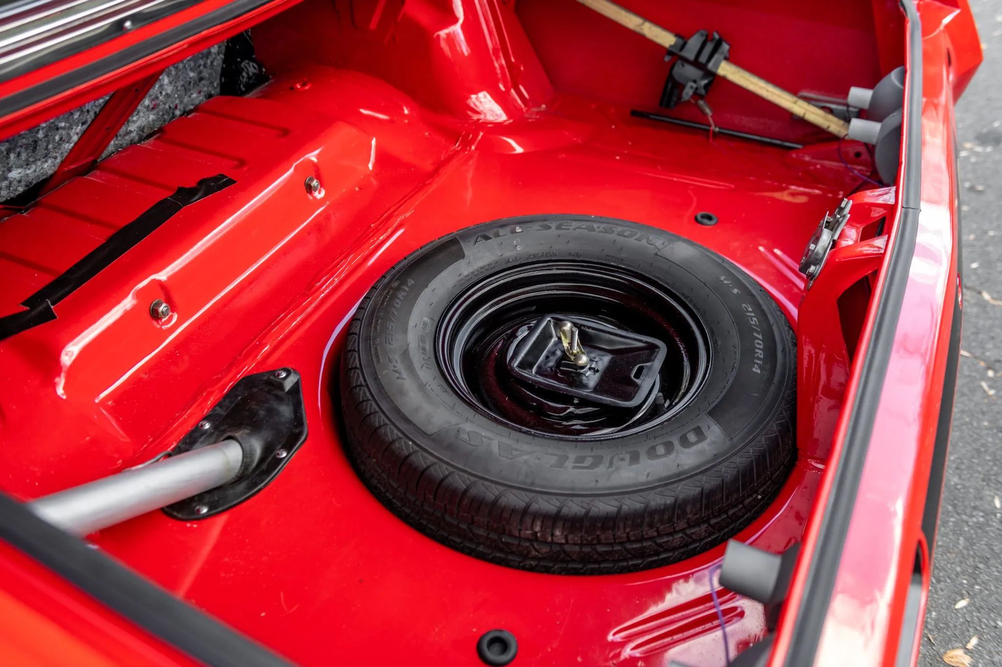 Trunk of a red 1970 Plymouth Duster with the trunk mat removed to expose the fuel filler and spare tire