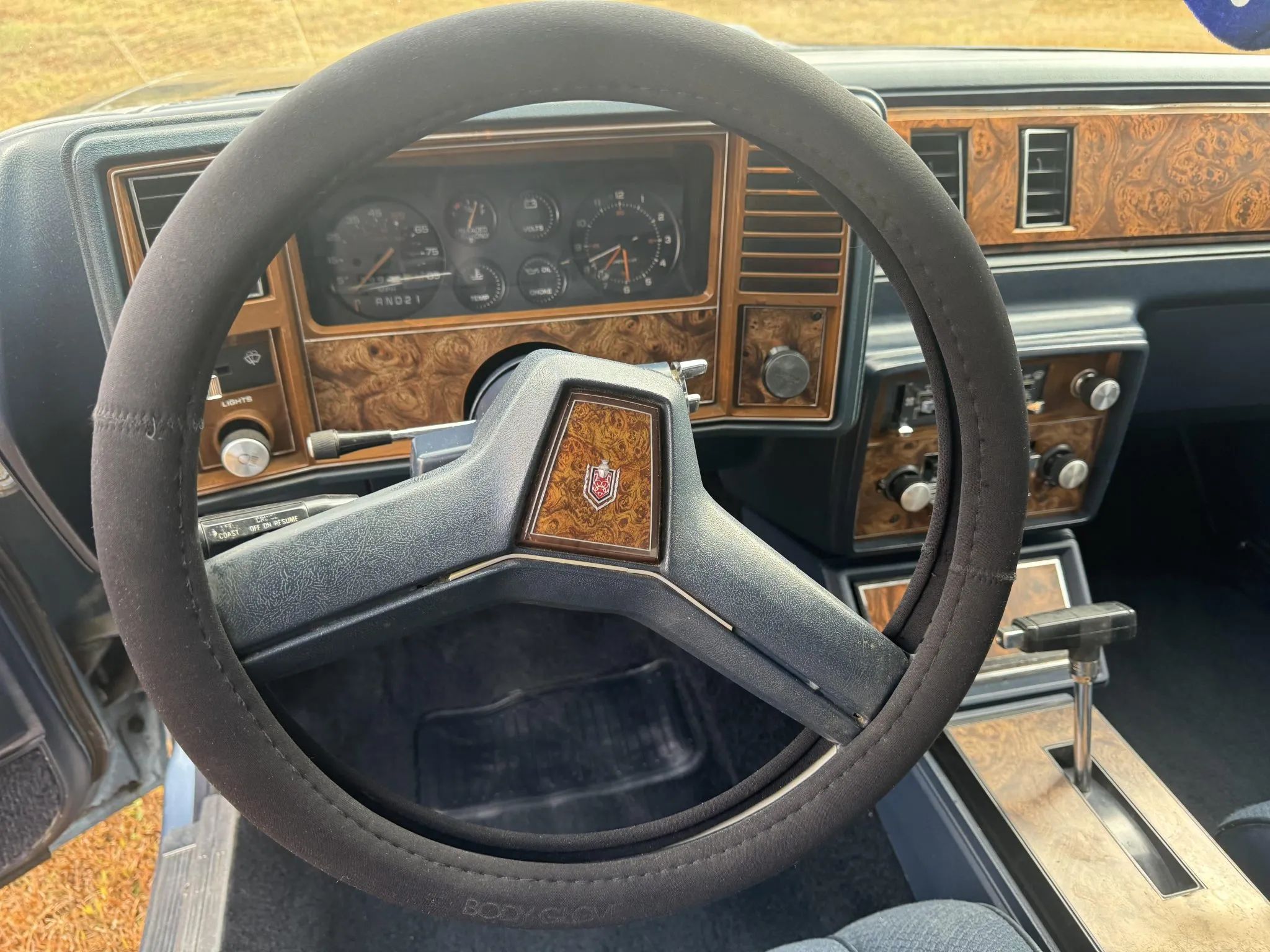 Rare Survivor: 1981 Chevrolet Monte Carlo Turbo V6 – Forgotten Chevy Still In Great Shape 12 Dashboard and steering wheel of a 1981 Chevrolet Monte Carlo with a blue interior and center console. The wheel has a steering wheel cover.