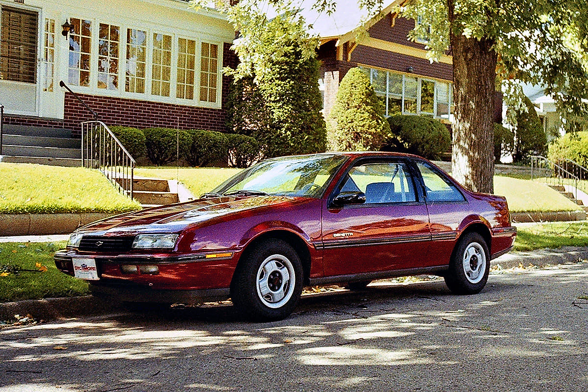 A red 1989 Chevrolet Beretta parked by the curbside. 