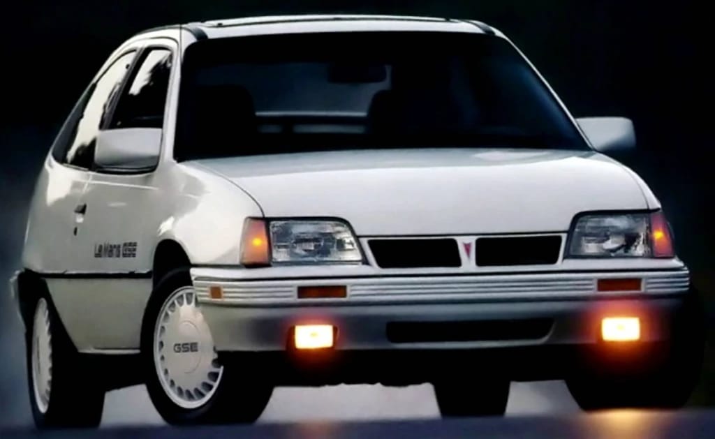 Press photo showing the front view of a white 1990 Pontiac LeMans with foglamps on