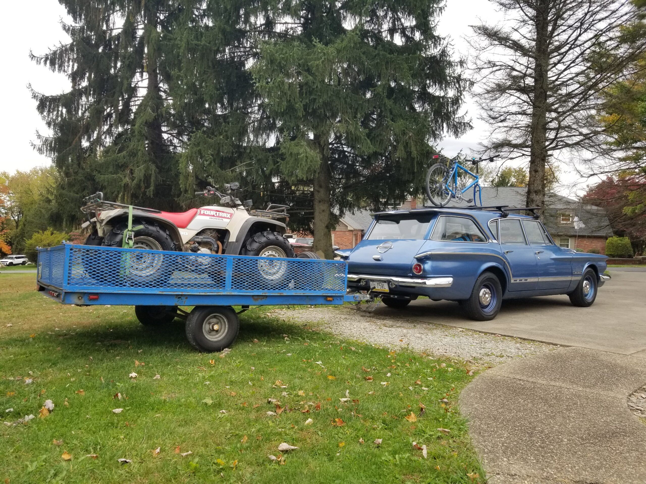 Photo of a blue 1962 Plymouth Valiant with a bicycle on its roof, towing a trailer with a four-wheel ATV