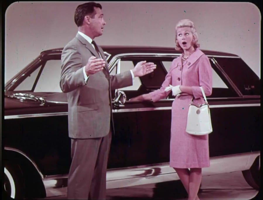 Classic Dealer Filmstrip: Selling The 1965 Chrysler — All The Facts, Just A Little Mansplaining 2 Photo of dealer filmstrip with sales prospect and salesman standing in front of a 1965 Chrysler New Yorker in black