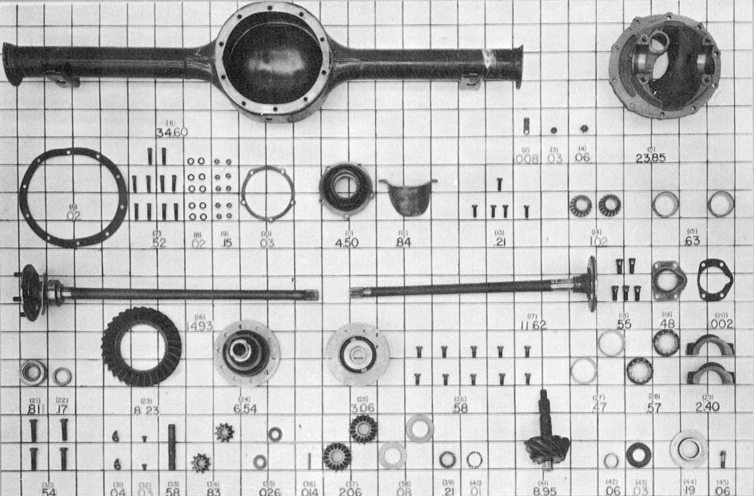 B&W photo of axle parts laid out on a mat, which is marked with the weight of each component