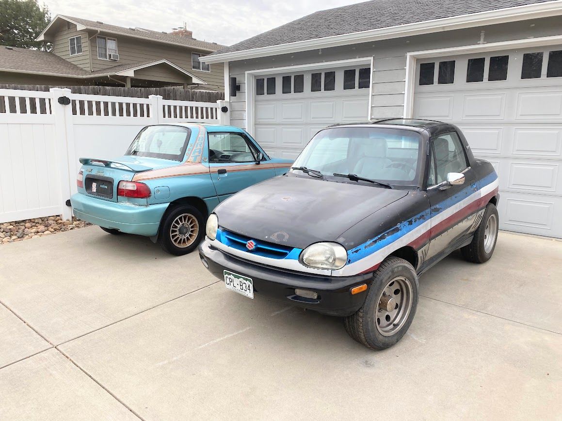 Photo of two Suzuki X-90 mini-SUVs, one in metallic blue with pink trim and "BRAT" decals, the other black with red, white, and blue stripes