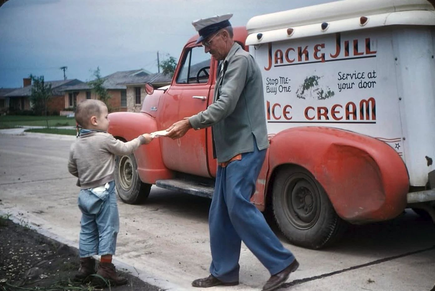 Photo of a uniformed ice cream man accepting a dollar from a young boy in front of a Jack & Jill Ice Cream Truck, a 1952 Chevrolet 3100 with a dented fender