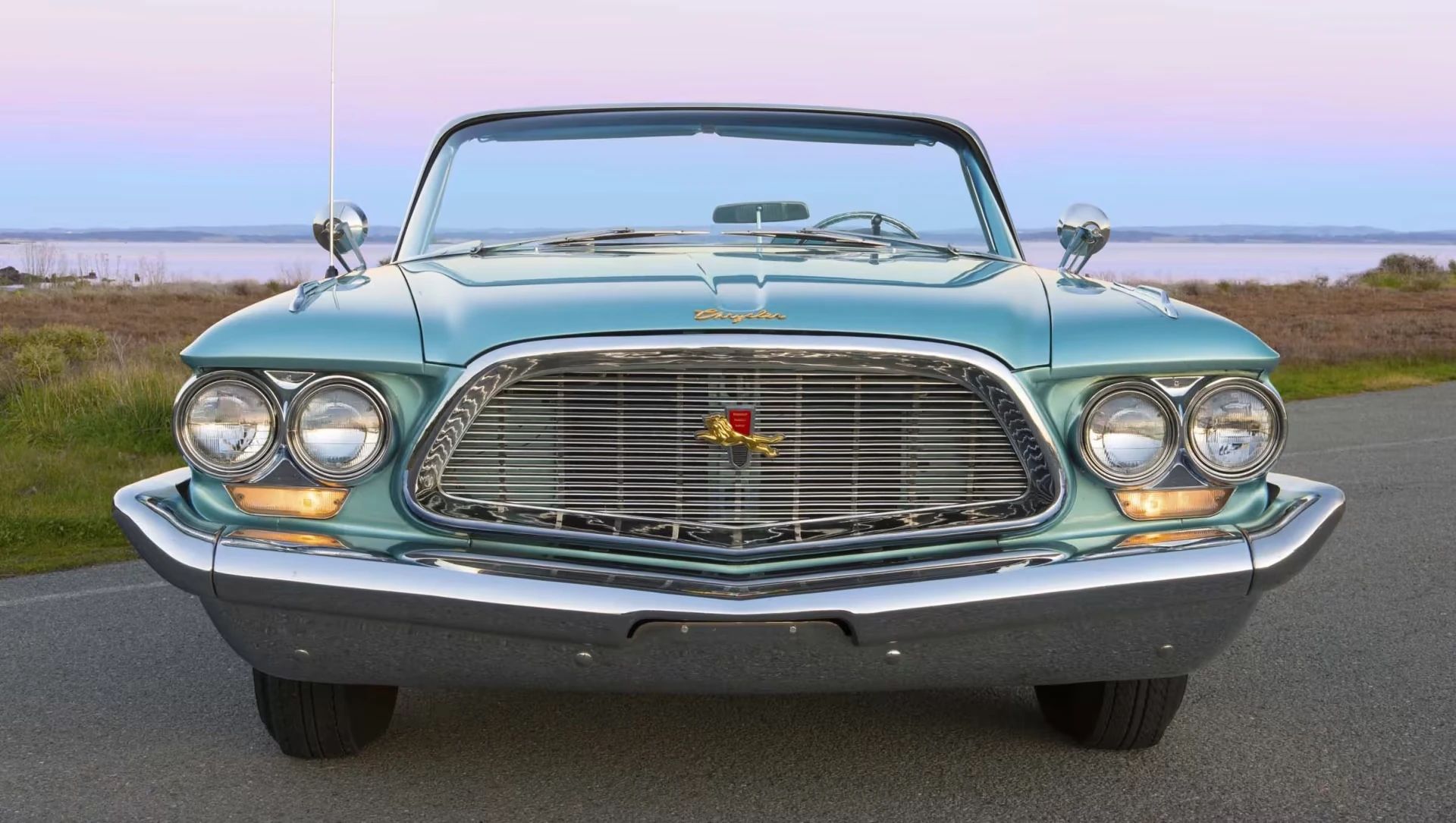 Front view of a turquoise 1960 Chrysler New Yorker with a dramatic sunset in the background