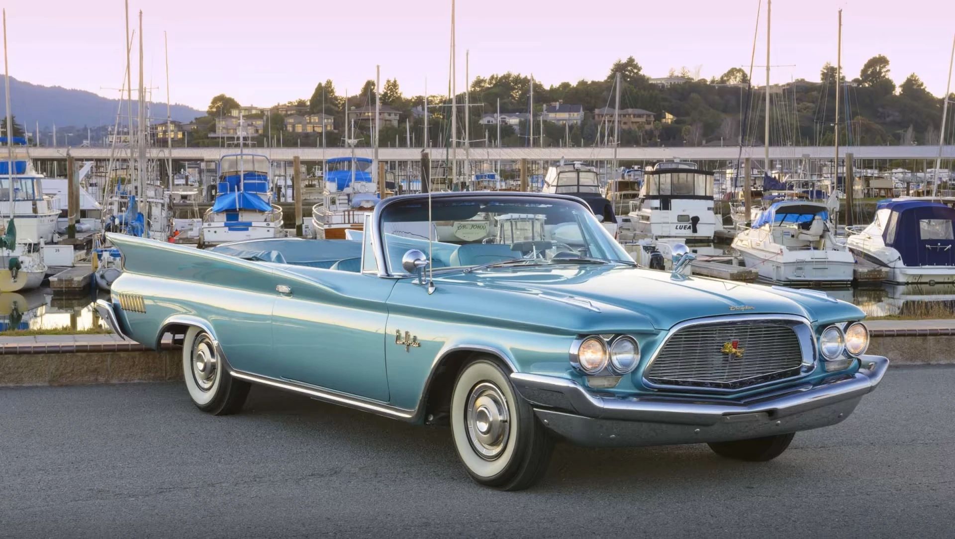 Right front 3q view of a turquoise 1960 Chrysler New Yorker convertible in front of a marina at sunset
