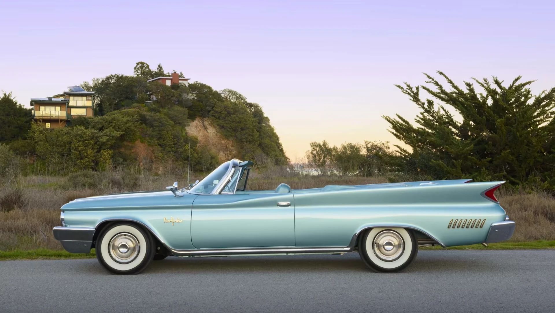 Left side view of a turquoise 1960 Chrysler New Yorker with a dramatic sunset in the background
