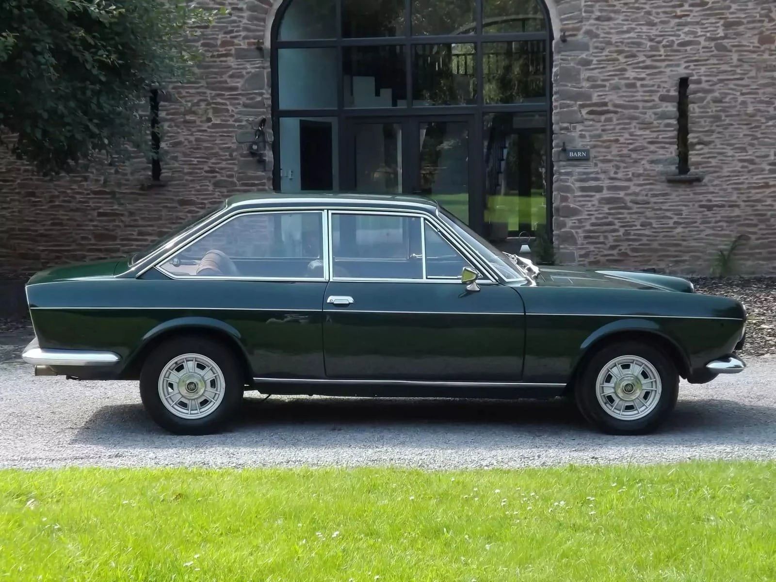 Right side view of a dark green 1968 Fiat 124 coupe