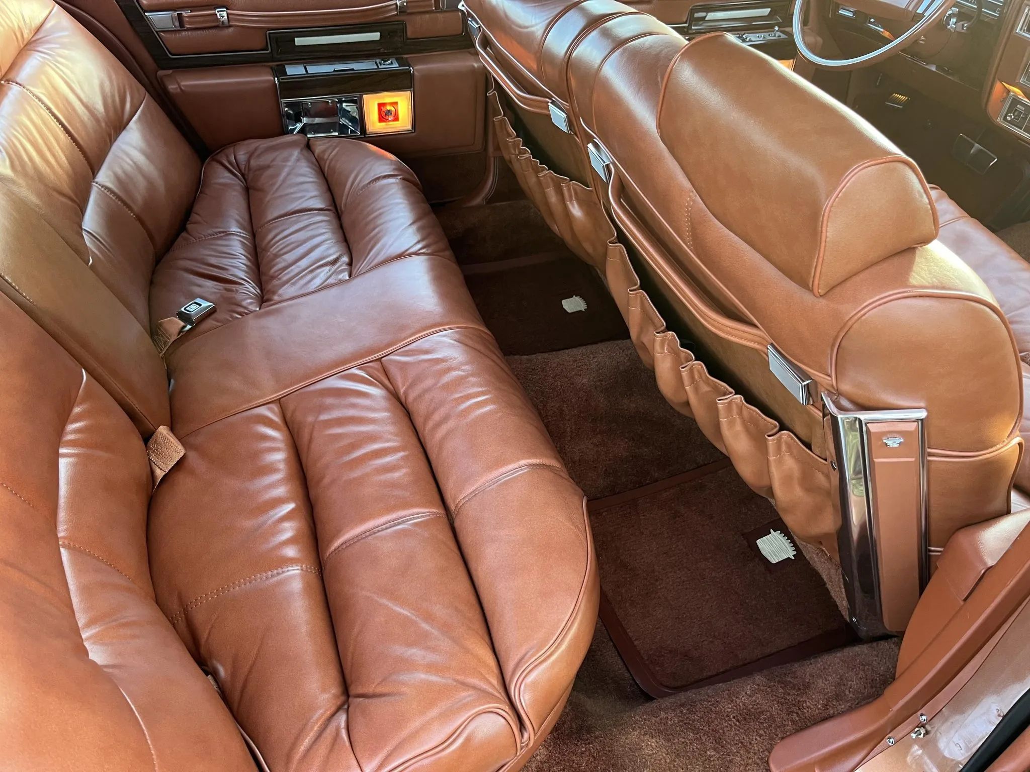 Back seat of a 1977 Cadillac Fleetwood Brougham with orange leather upholstery and seat-back map pockets