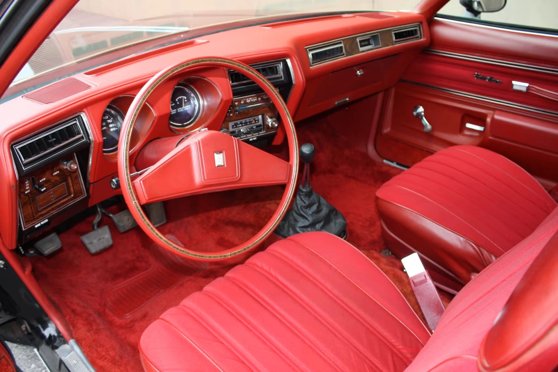 Dashboard of a 1977 Oldsmobile Cutlass Supreme with a red interior and bucket seats