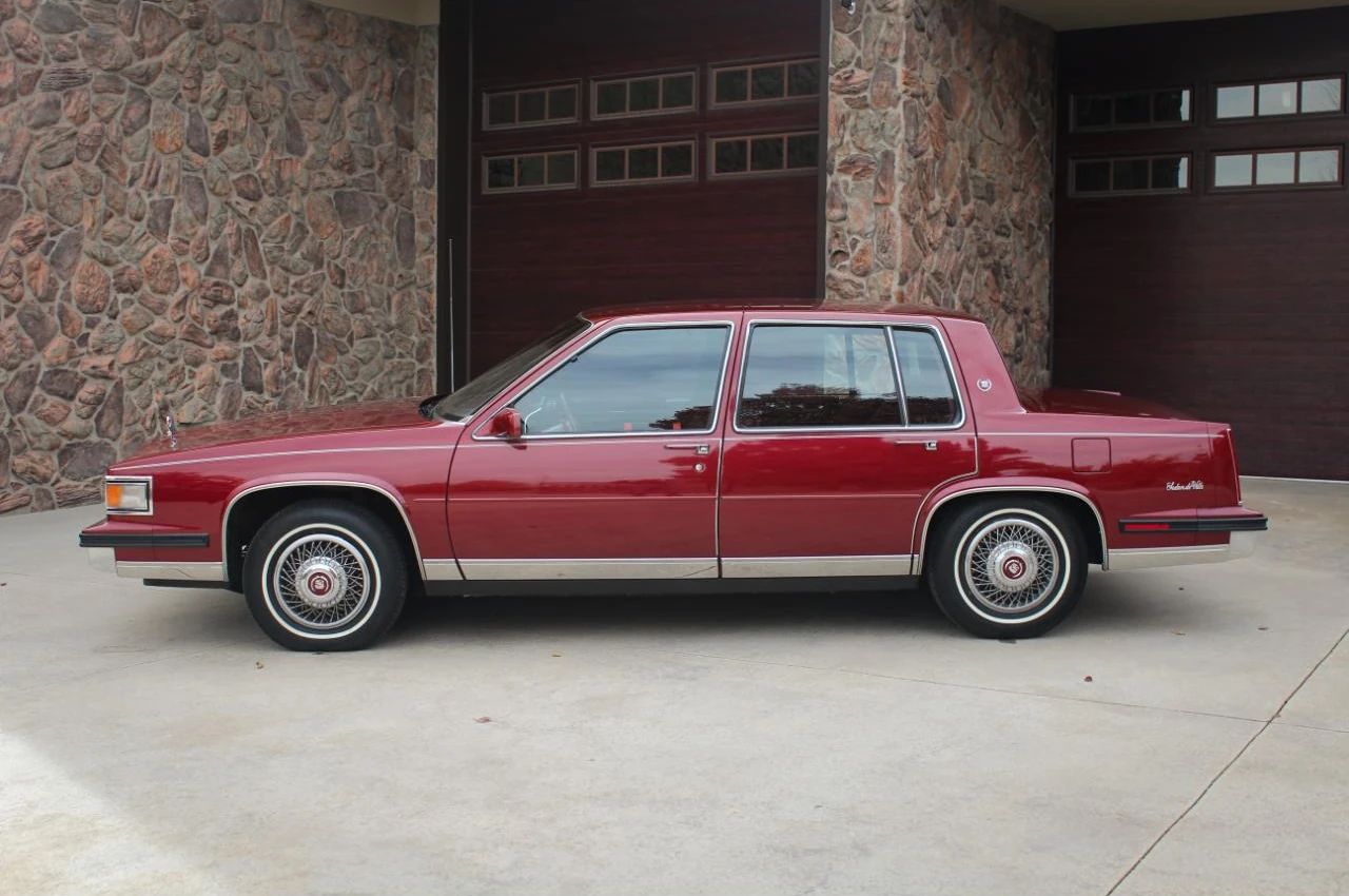 Left side view of a red 1985 Cadillac Sedan de Ville four-door sedan