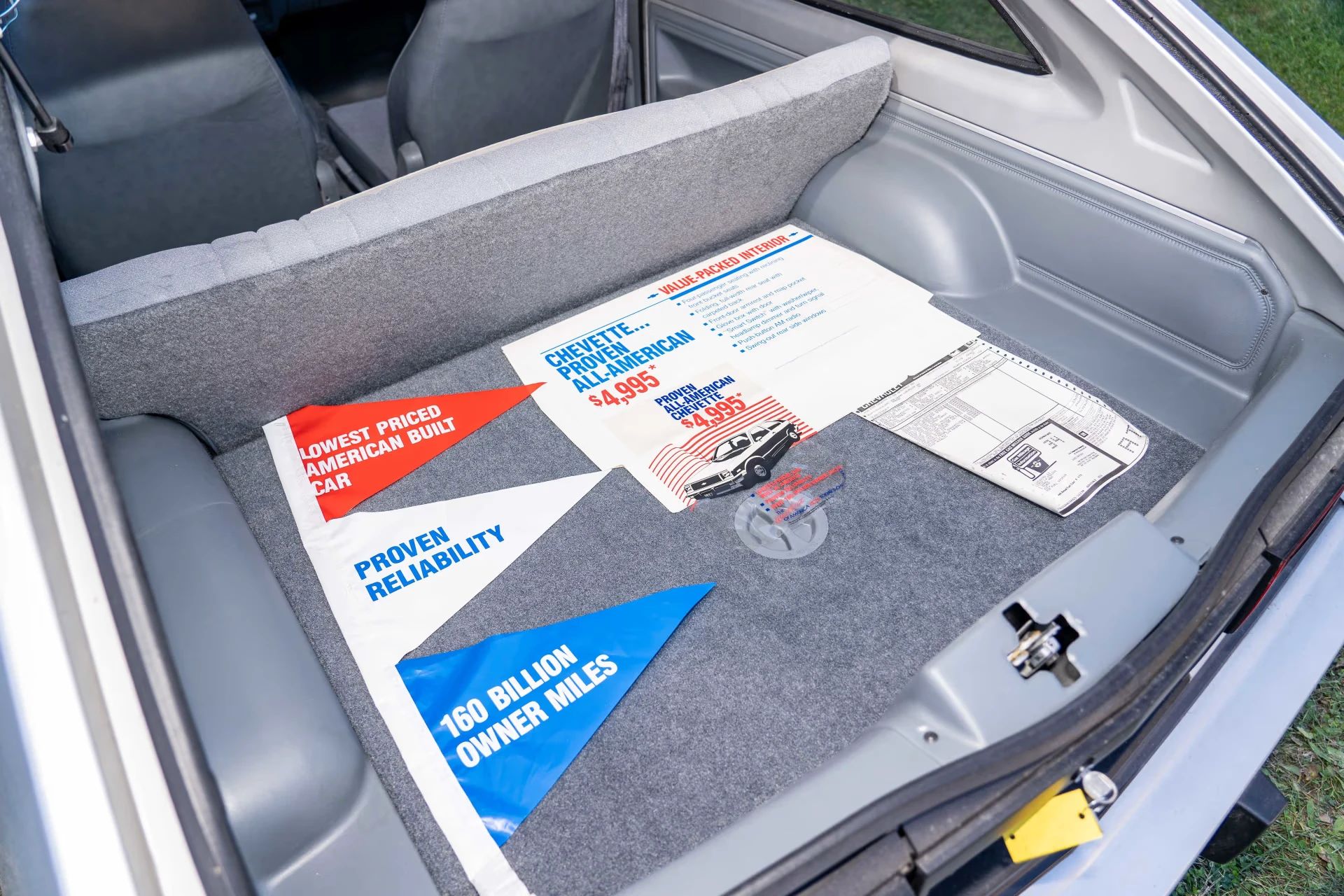 Trunk of a 1987 Chevrolet Chevette with an old dealer sign advertising its $4,995 base price