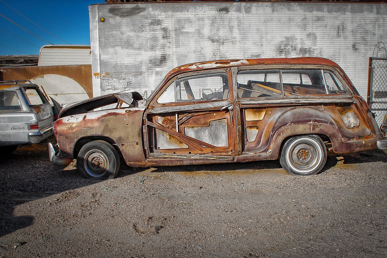 Skeletal remains of a rusty 1949-1951 Ford station wagon, with all of its wood exterior panels gone