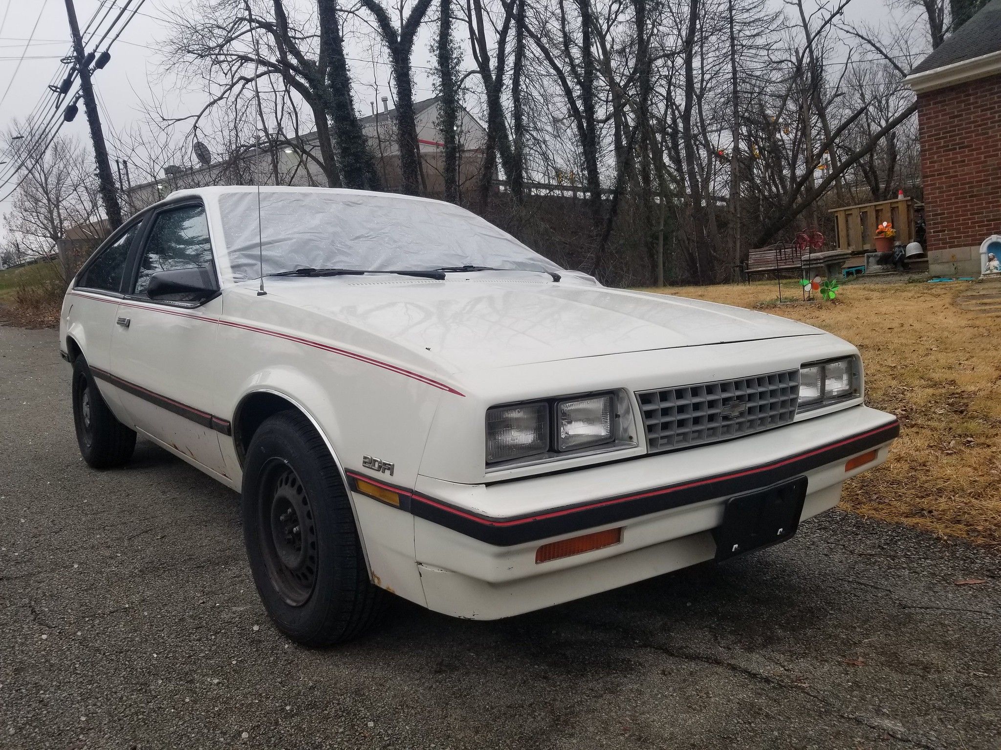 1986 Chevrolet Cavalier CS Hatchback: "America's Favorite Car" 9 Picture of front-passenger three-quarter view of a 1986 Chevy Cavalier CS hatchback in white in front of a modest brick home