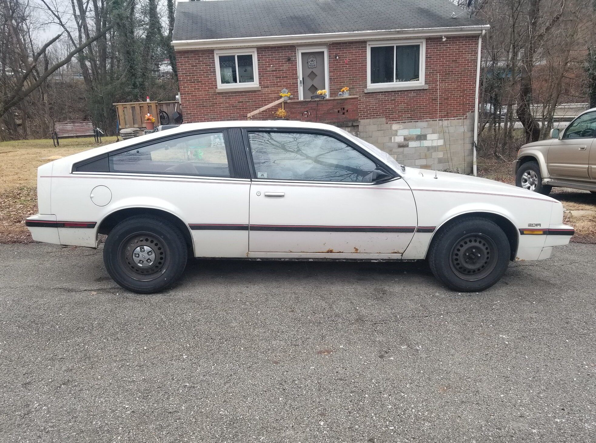 1986 Chevrolet Cavalier CS Hatchback: "America's Favorite Car" 1 Image of the profile of a white 1986 Chevy Cavalier CS hatchback parked in front of a nice, small brick home on a chilly day