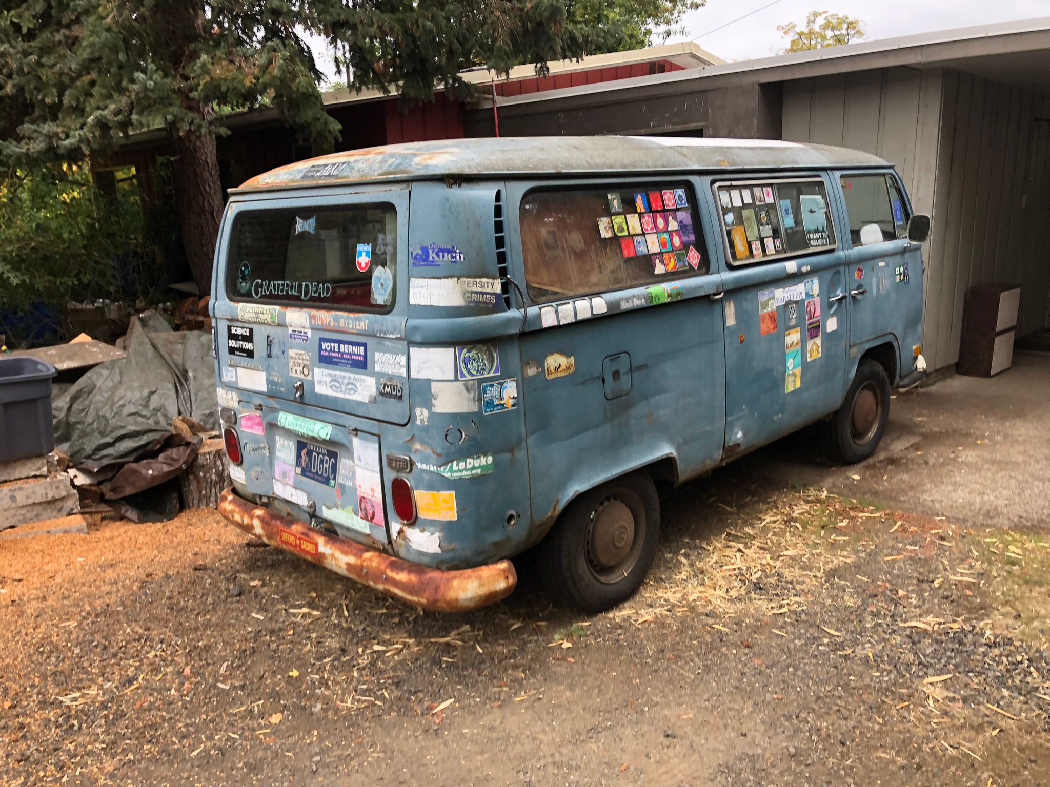 Photo of a faded blue Volkswagen Type 2 with rusted bumpers, covered in stickers