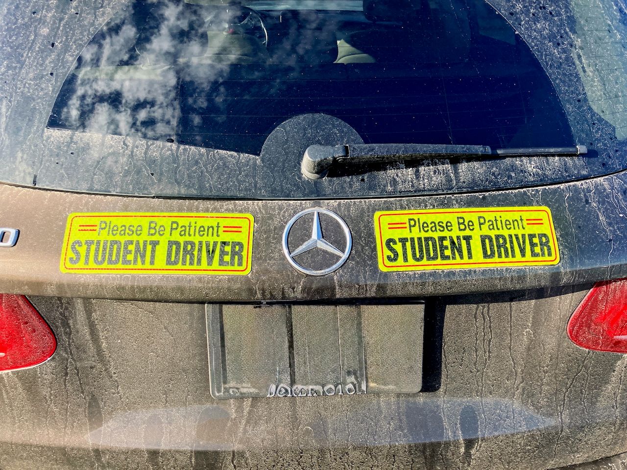 Car Warning Stickers: Embarrassment, Safety, or What 1 Back window of a dusty Mercedes-Benz with bumper stickers reading "Please Be Patient: STUDENT DRIVER"