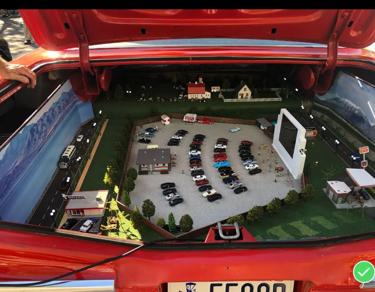 A miniature diorama with a drive-in theater and a bunch of little scale-model cars, installed in the trunk of a red Chevrolet