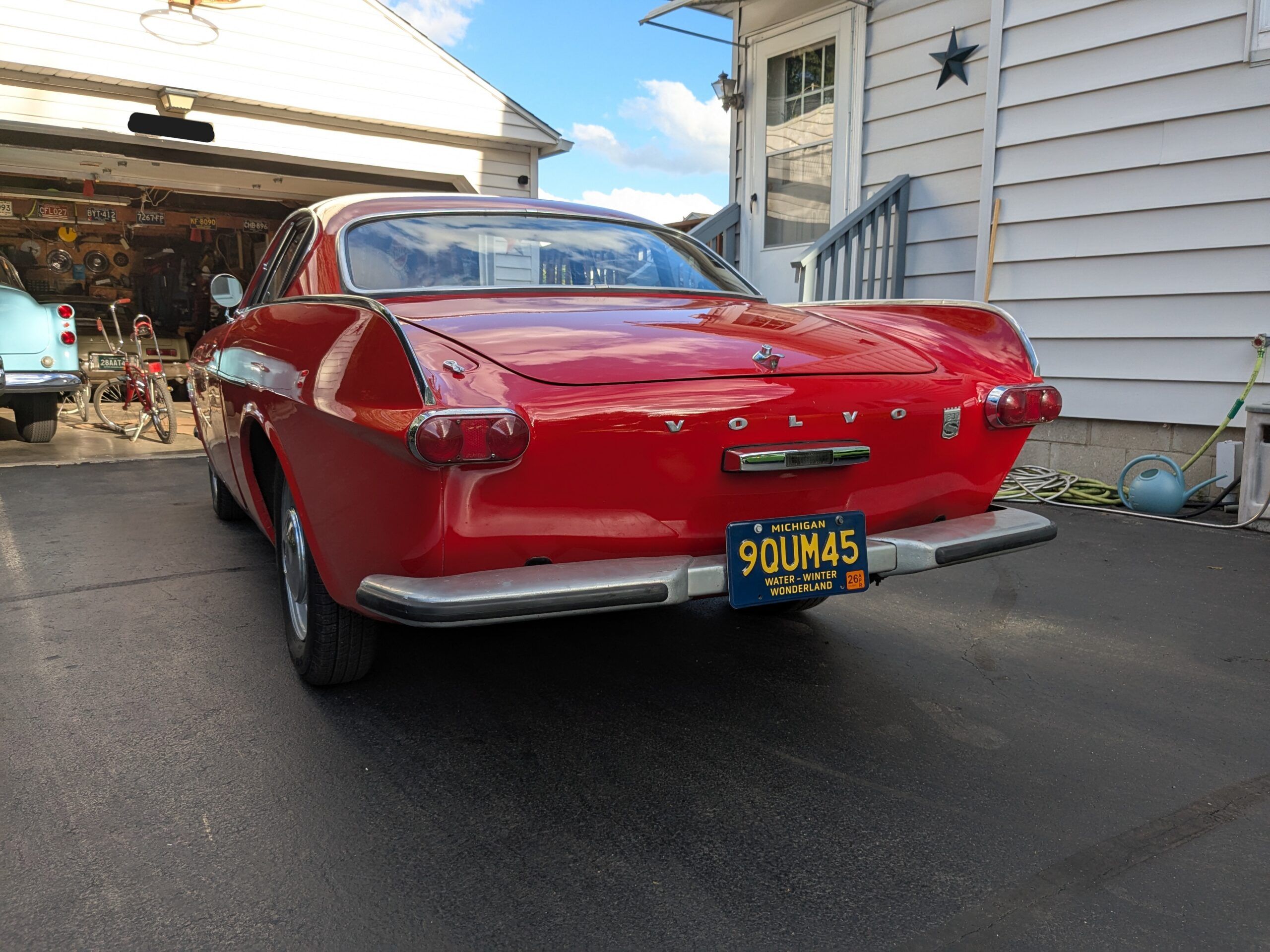 Picture of Signal Red 1967 Volvo 1800 parked in a residential driveway with classic Buicks in the garage in the background