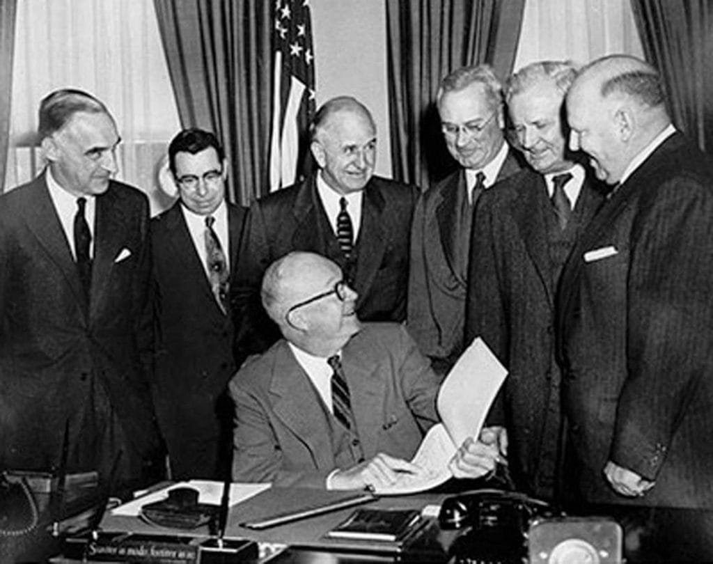 Photo of Dwight D. Eisenhower in the Oval Office, surrounded by men in suits