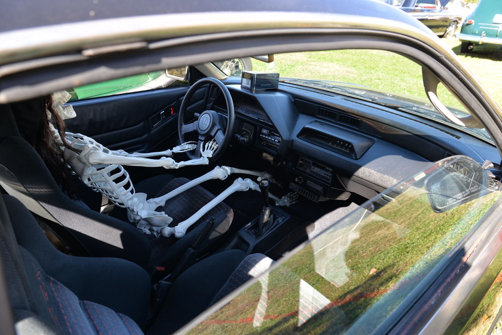 Interior of a black LHD 1985 Honda CRX with a plastic skeleton behind the wheel