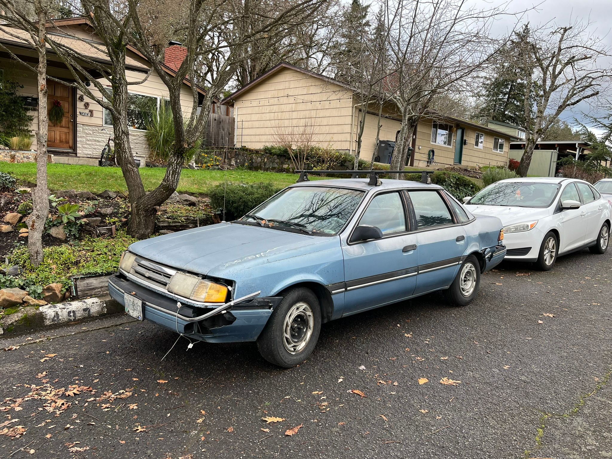 Battered blue 1989 Ford Tempo four-door sedan parked at the curb