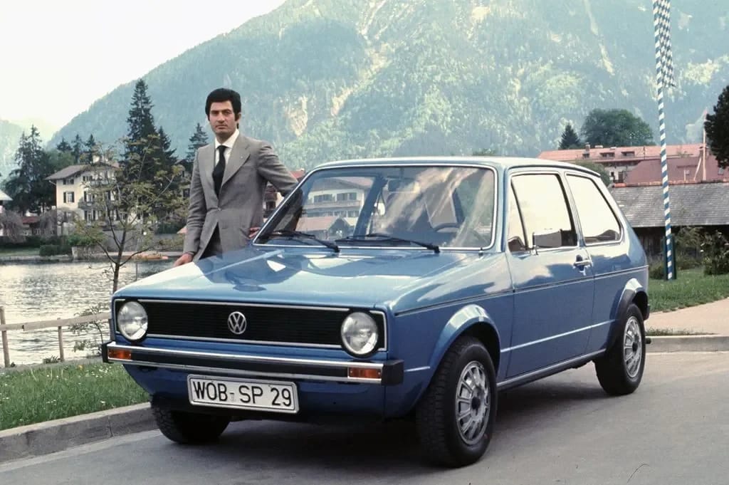 Photo of a man in a suit standing by a blue 1974 VW Golf 3-door
