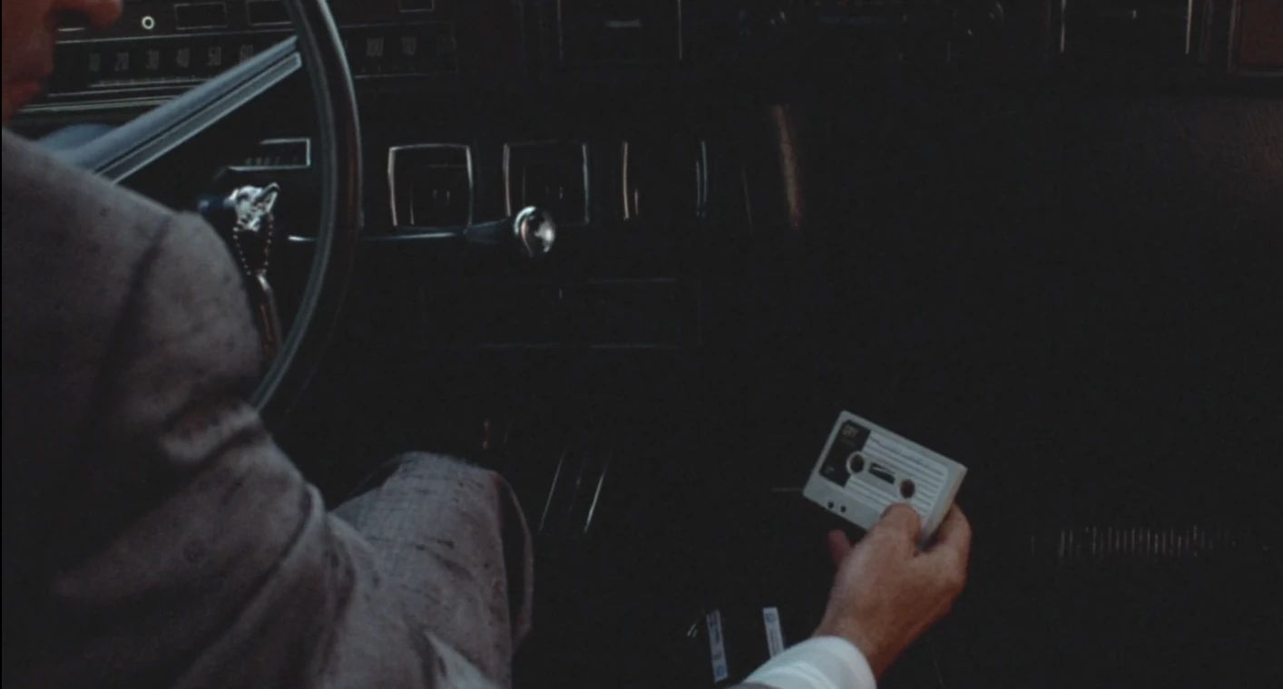 Why The 1972 Lincoln Continental Was The Perfect Movie Costar In This Jack Lemmon Drama 9 Movie screenshot of a hand holding a cassette tape in the interior of a 1972 Lincoln