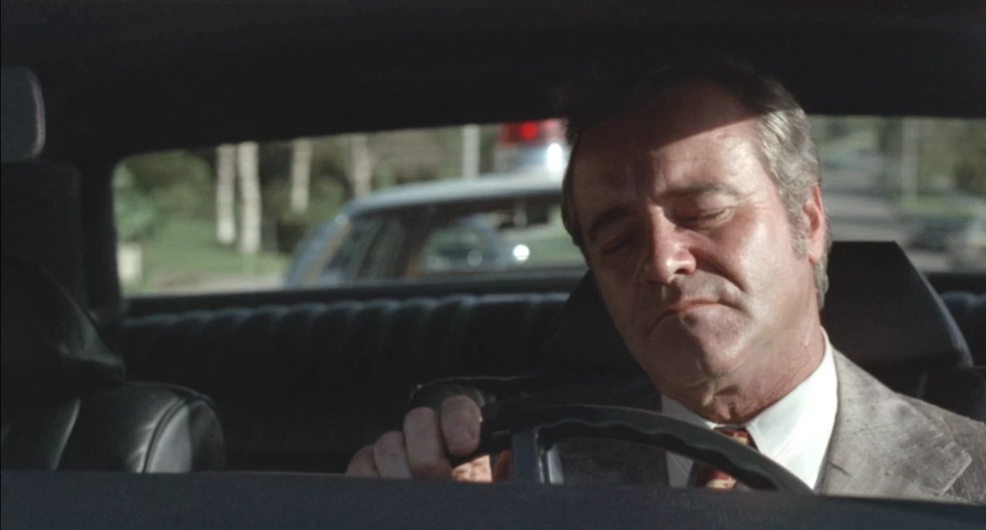 Why The 1972 Lincoln Continental Was The Perfect Movie Costar In This Jack Lemmon Drama 8 Movie still of Jack Lemmon behind the wheel of a Lincoln, eyes closed, looking happy, with a police car visible through the back window
